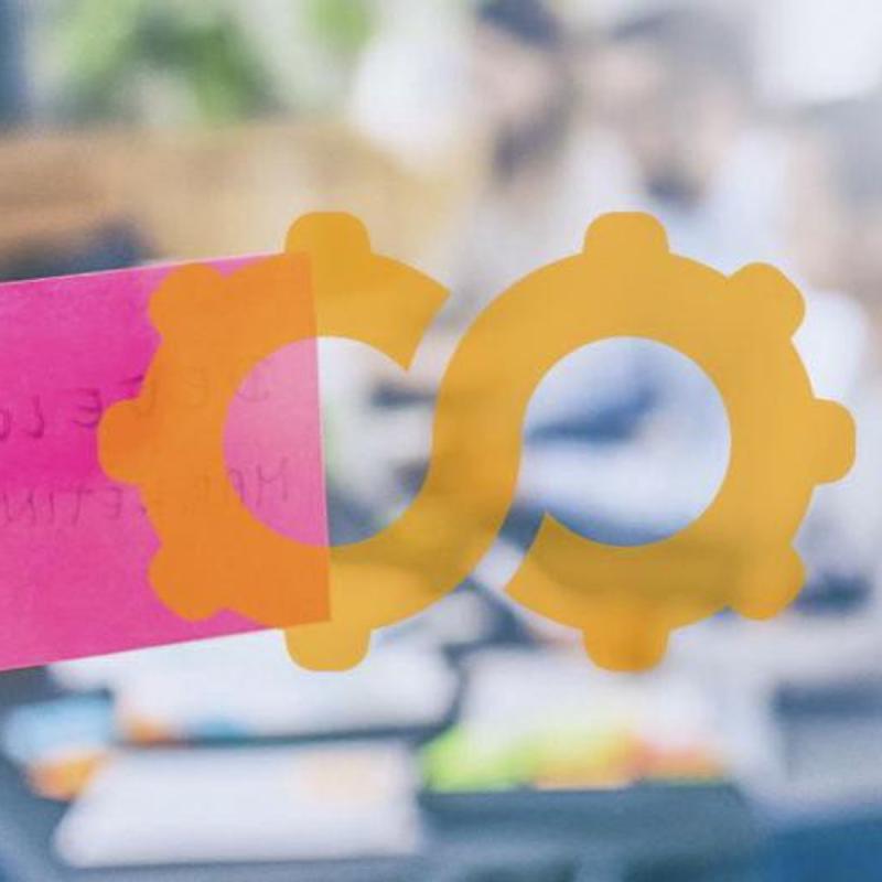 Two translucent orange gears forming an infinity symbol on a window, with a pink sticky note behind them